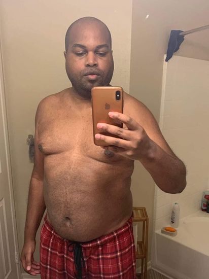 A shirtless man is taking a selfie in a bathroom with his phone.