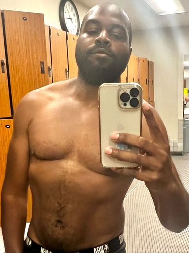 A shirtless man is taking a selfie in a locker room.