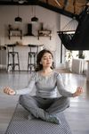 A woman is sitting in a lotus position on a yoga mat in a living room.