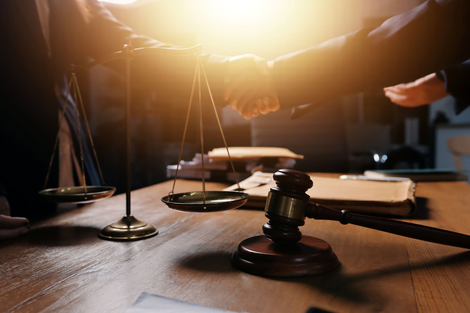Gavel and scales on desk, two people shake hands, sunlight.