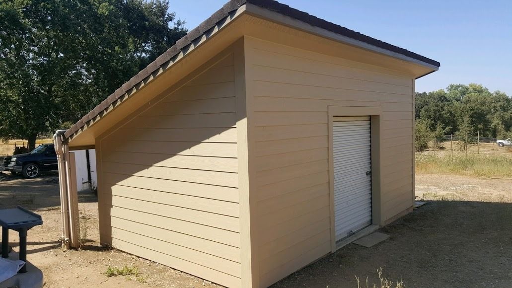 Tan building with a slanted roof, white door, and adjacent informational sign; outdoors on a sunny day.