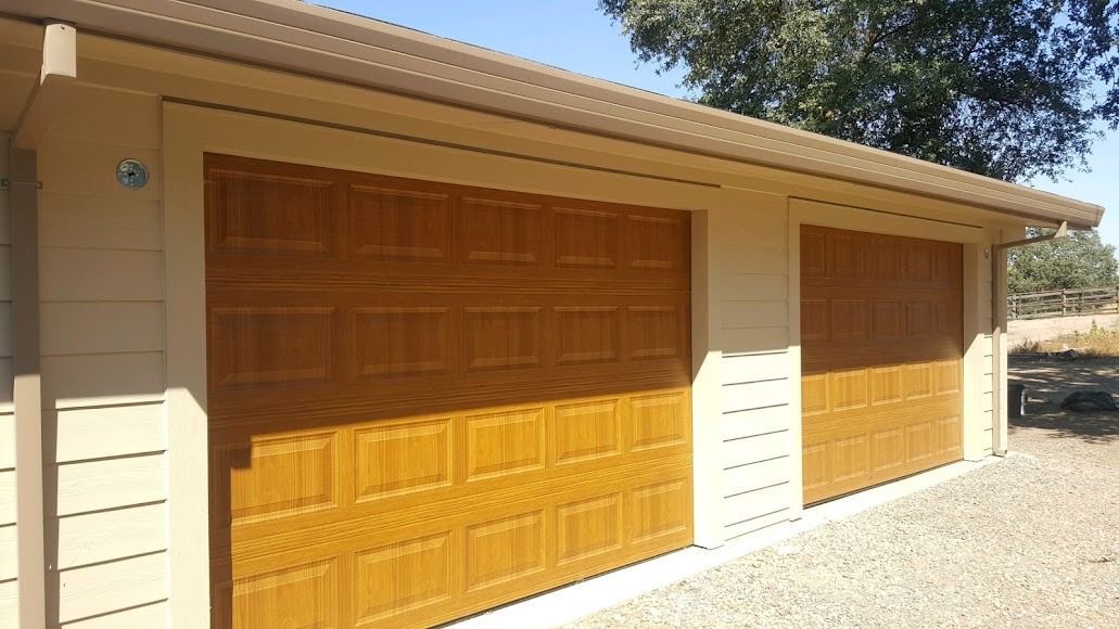 Two tan garage doors on a beige building under a brown roof.