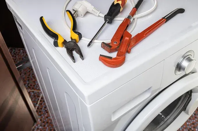 Tools (pliers, screwdriver, wrench) on top of a white washing machine, ready for repair.