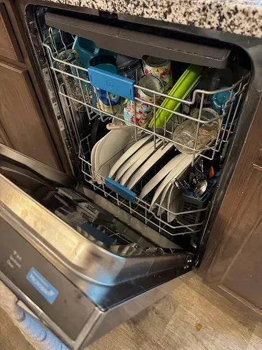 Dishwasher with open door, loaded with dishes. Silver interior, blue accents, filled with plates and glassware.