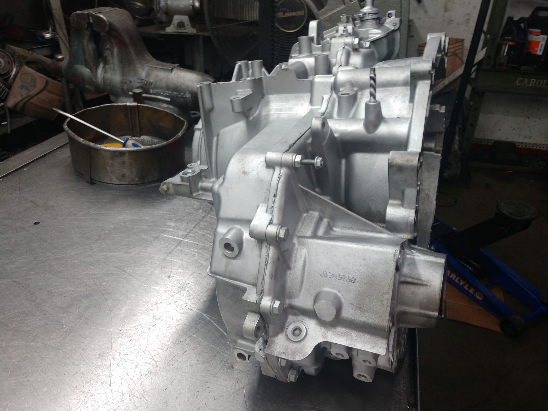 Silver metal gearbox on a workshop floor beside a bucket and automotive parts