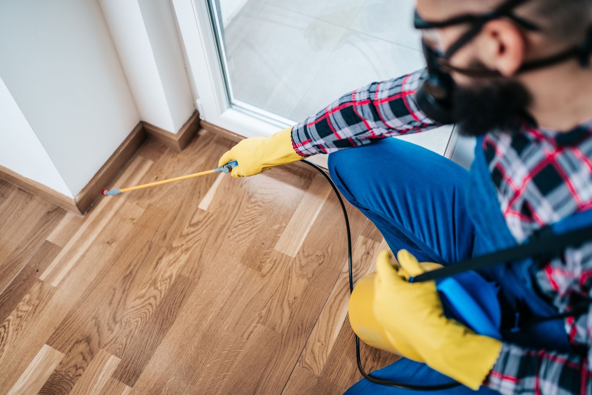 An exterminator, from a pest control company, in protective workwear, is spraying pesticide indoors. An exterminator, from a pest control company, in protective workwear, is spraying pesticide indoors.