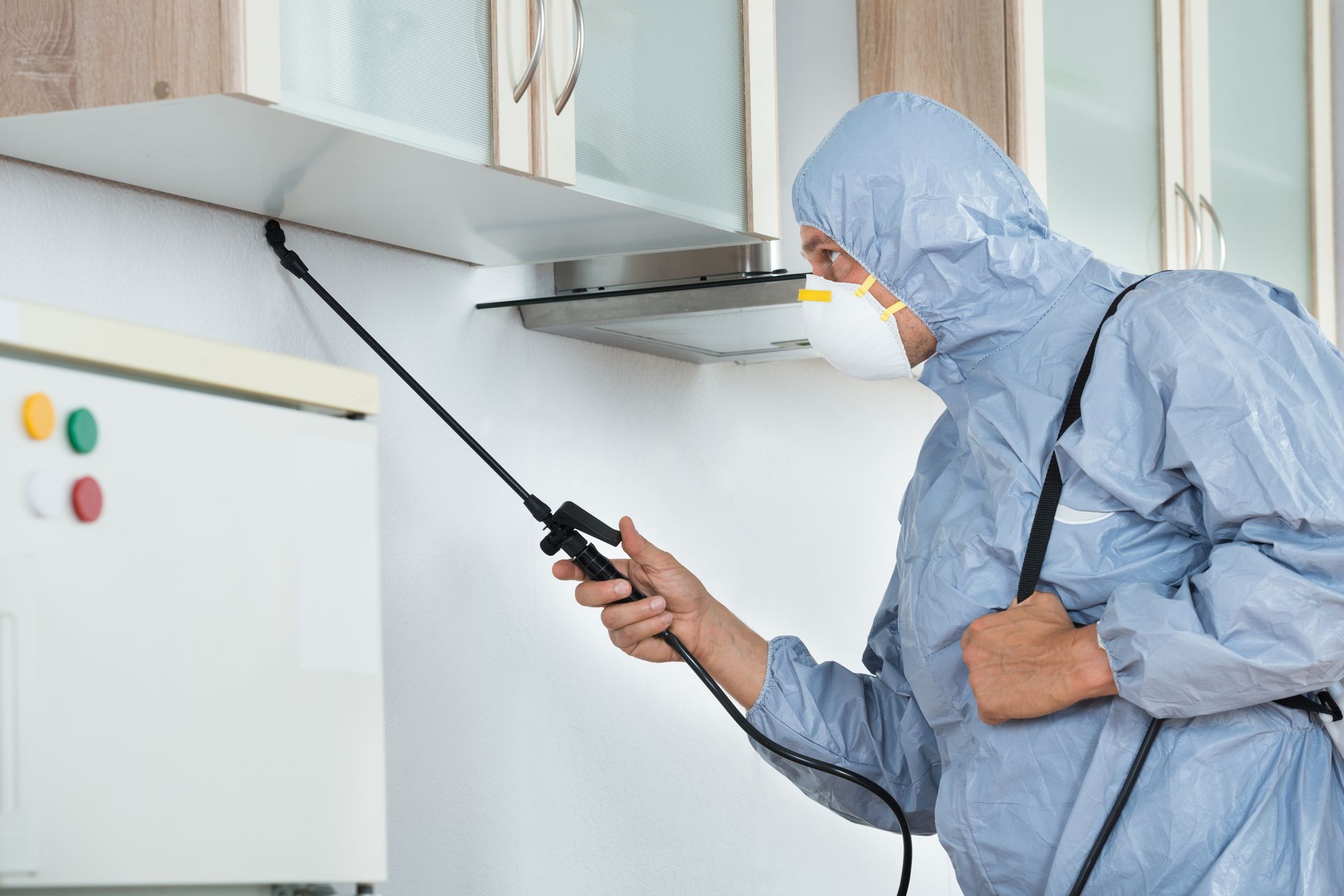 Pest exterminator in protective gear sprays a kitchen in Rochester, NY, ensuring a pest-free environ