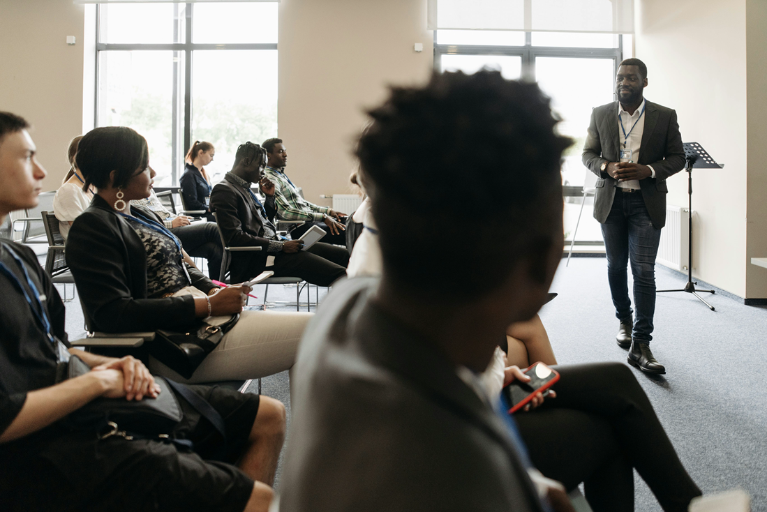 Speaker presenting to seated audience in a bright conference room