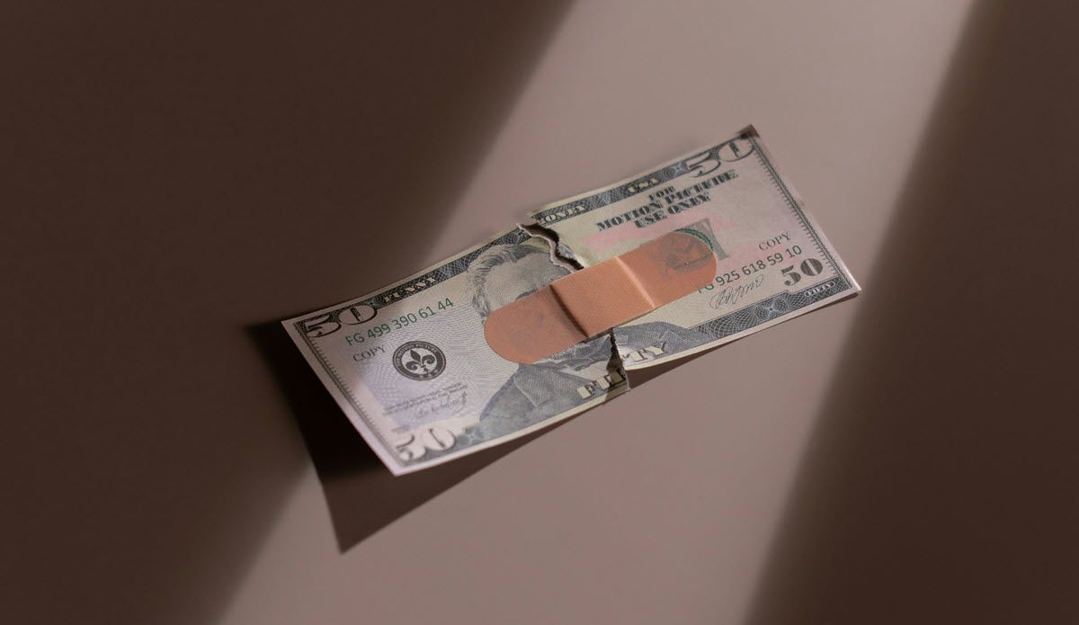 Two folded dollar bills with a band across the middle, lying on a table in warm light.