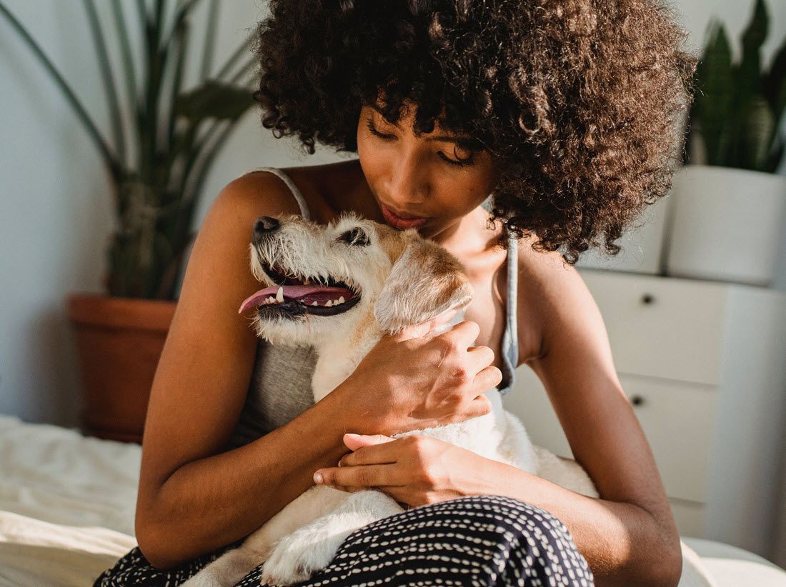 Woman cuddling a small white dog on a couch in a bright room