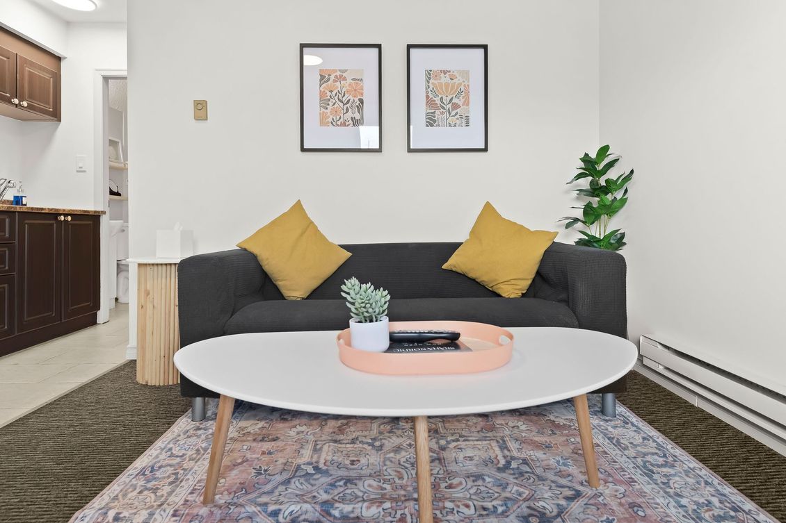 A modern living room with a dark grey sofa, yellow cushions, a white oval coffee table, and patterned area rug.