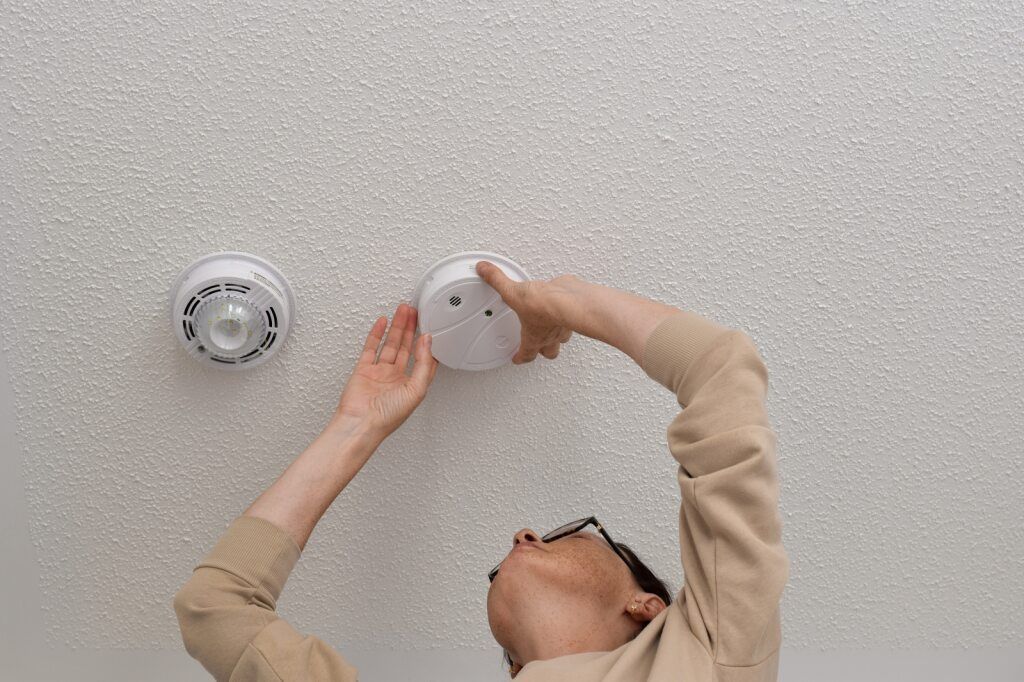 Person Installing or Checking a Smoke Detector on a White Textured Ceiling — AJW Electrical & Solar in Roma, QLD

