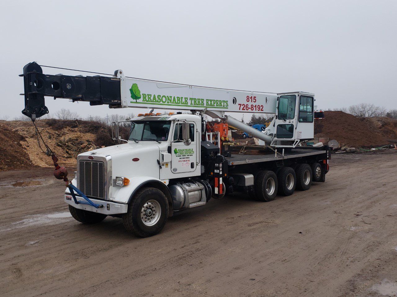 A large white truck with a crane on the back is parked on a dirt road.