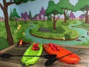 two kayaks and paddles are sitting on a wooden floor in front of a painting of a river .