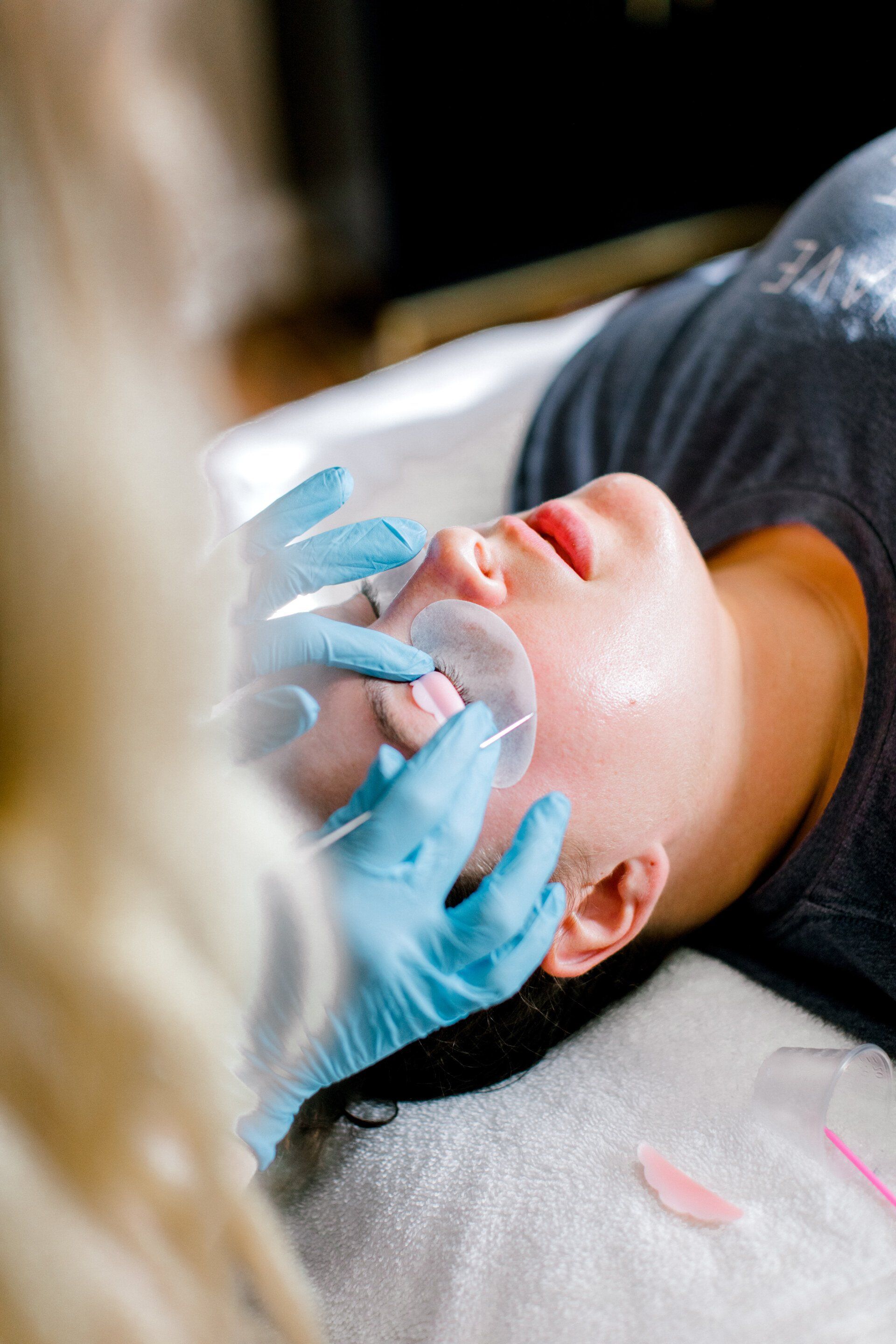 Woman receiving facial treatment; therapist wearing blue gloves massages her face with hands.