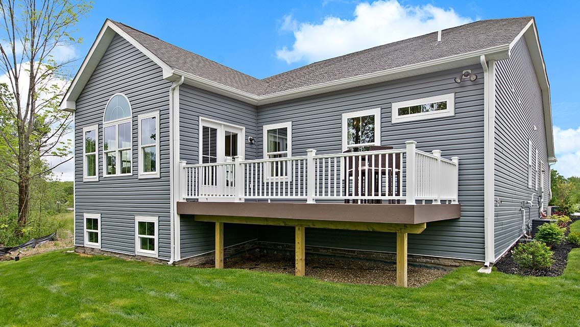 A gray house with a white deck and trim. Green grass surrounds the home under a blue sky.