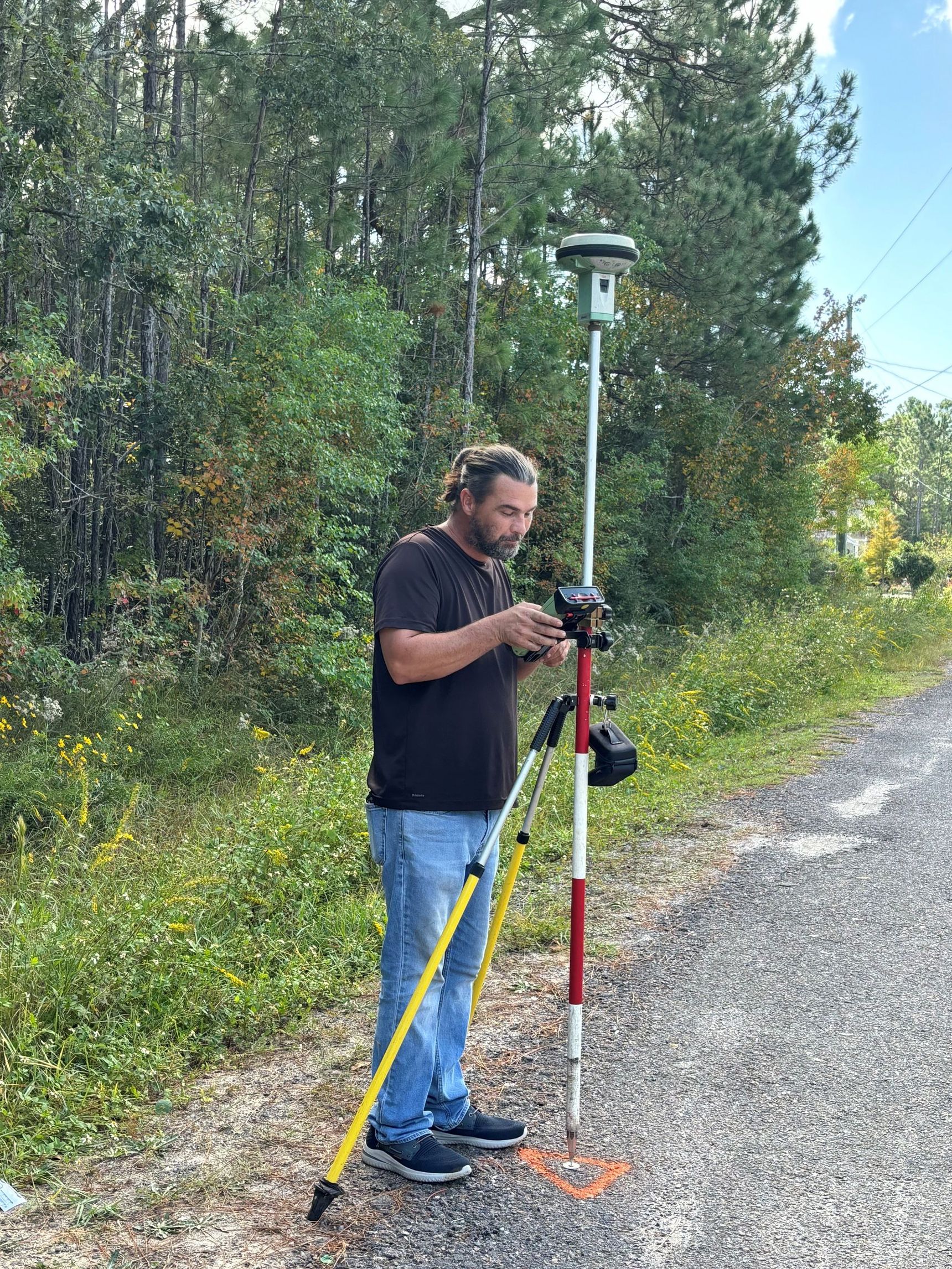 A man is standing next to a tripod on the side of a road.