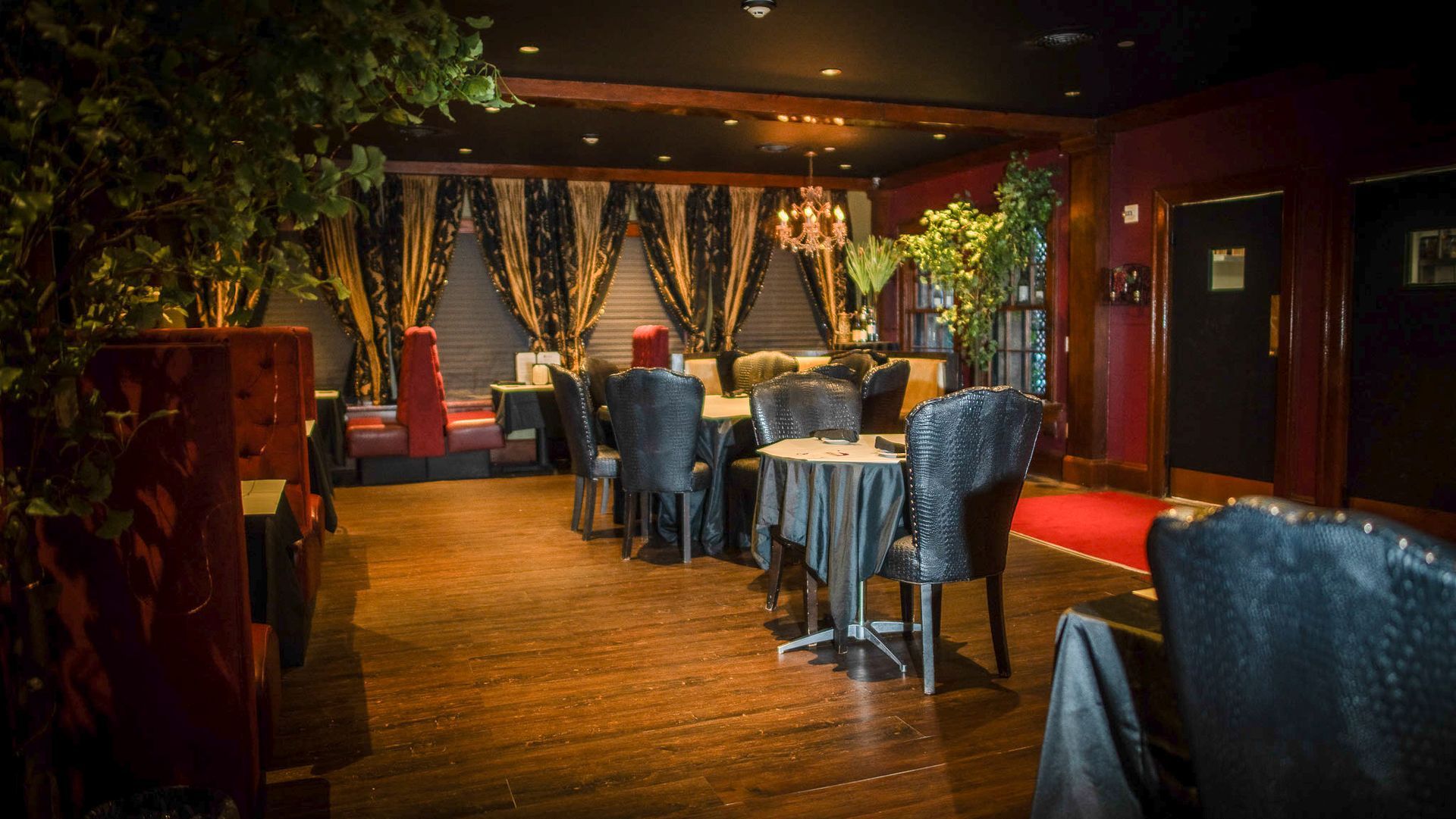 Interior view of a dimly lit restaurant with tables, chairs, and dark red walls.