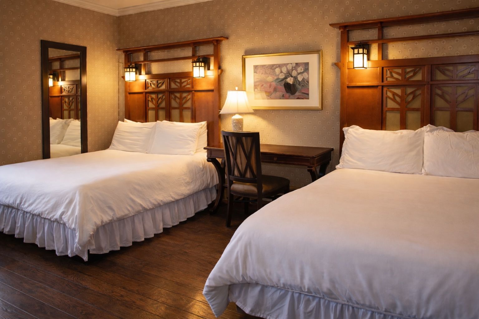 Two beds in a hotel room with dark wood headboards, desk, and mirror.