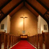 Interior of a church with a red carpet leading to an altar with a cross hanging above.