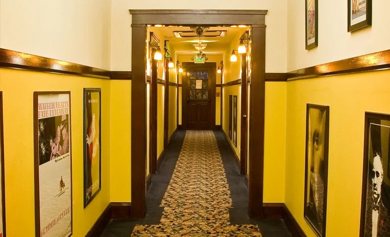 Yellow hallway with dark wood trim, framed posters, and a patterned rug.