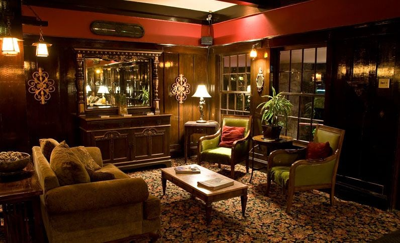 Cozy, dark-toned living room with antique furniture: couch, armchairs, coffee table, and large ornate mirror.