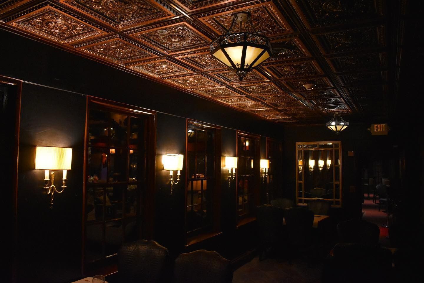 Dark, elegant room with ornate copper ceiling, wall sconces, mirrors, and seating.