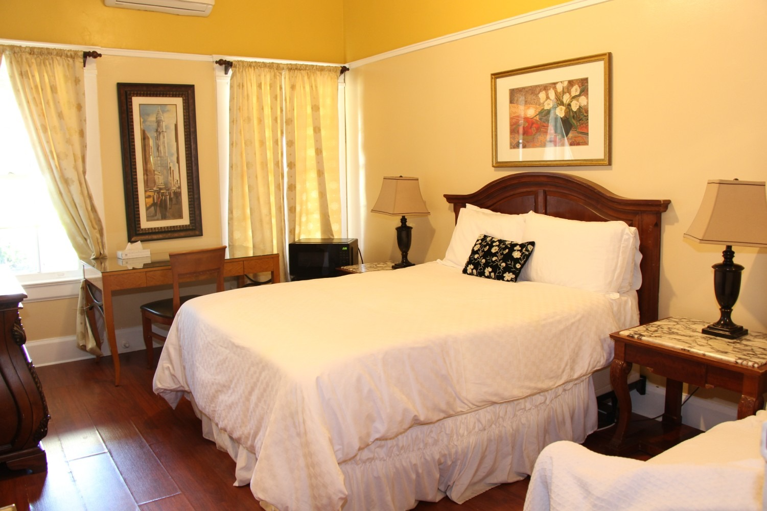 Bedroom with a made bed, nightstands with lamps, a desk, artwork, and curtains.