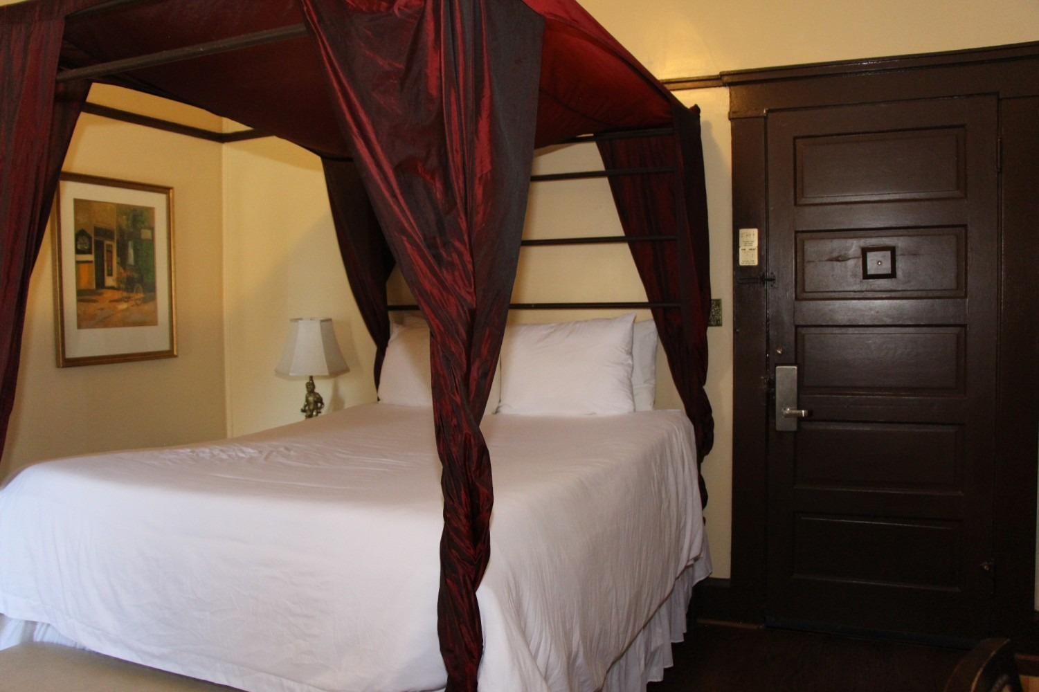 Bedroom with a canopy bed, red drapes, white bedding, and a dark brown door.