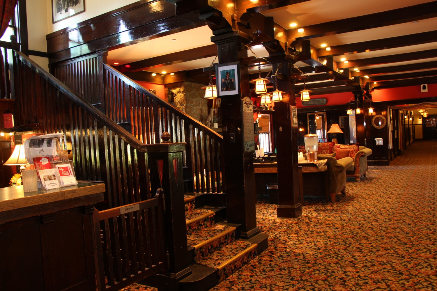 Wooden staircase and lobby in a dimly lit building with warm-toned lighting and patterned carpet.