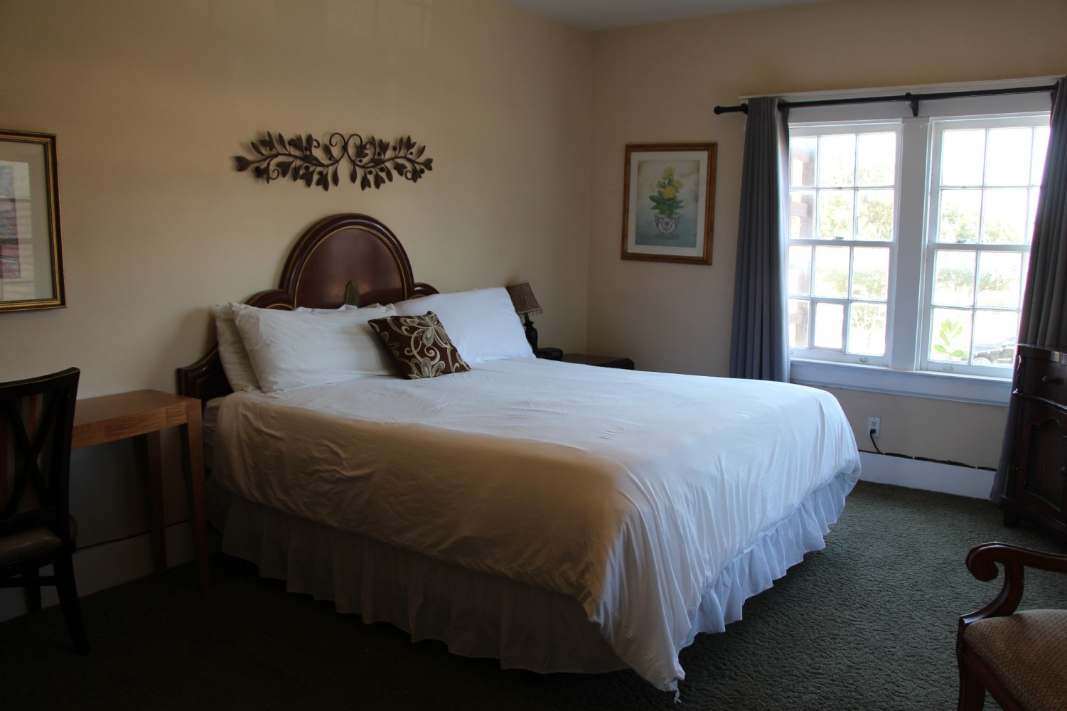 Bedroom with a bed, nightstands, and a window. Light beige walls with dark green carpet.