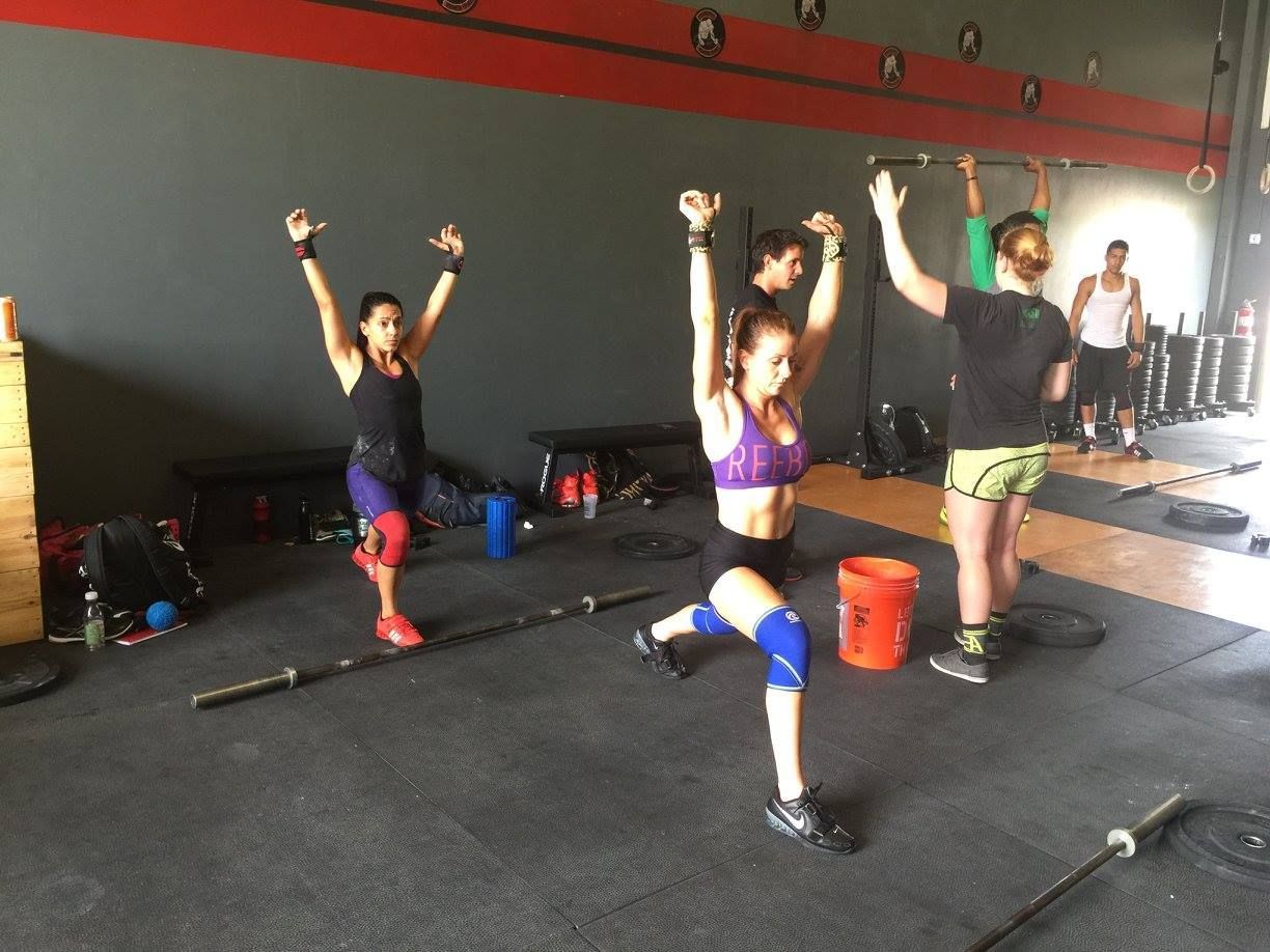 Three people performing lunges with arms raised in a gym setting.