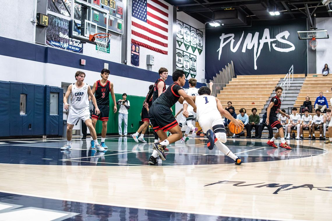 Basketball players in white and black uniforms compete during a game on an indoor court under a large 