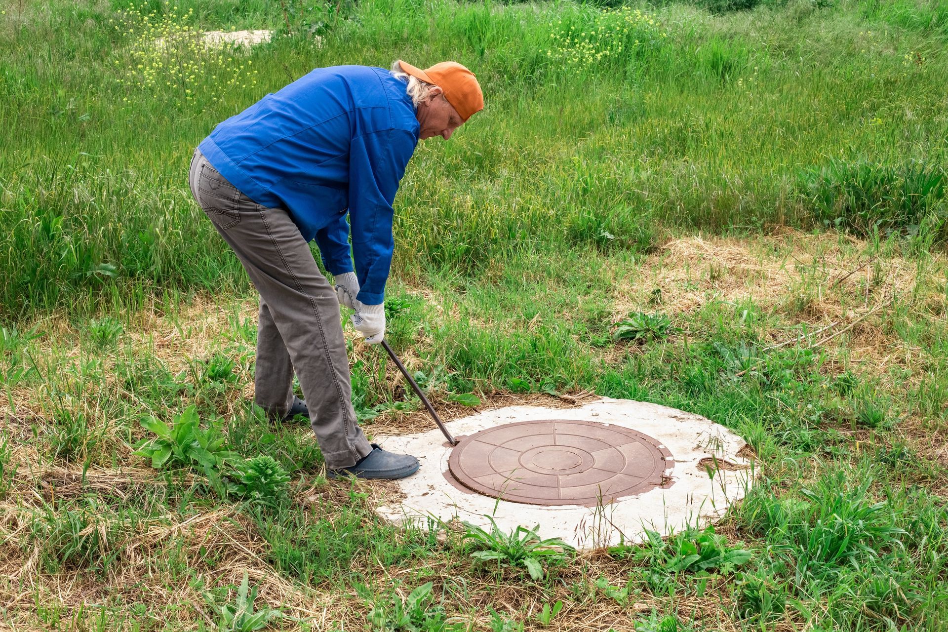 A man is looking into a manhole cover with a hammer.