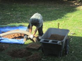 a man is using a vacuum hose to pump dirt into a wheelbarrow .