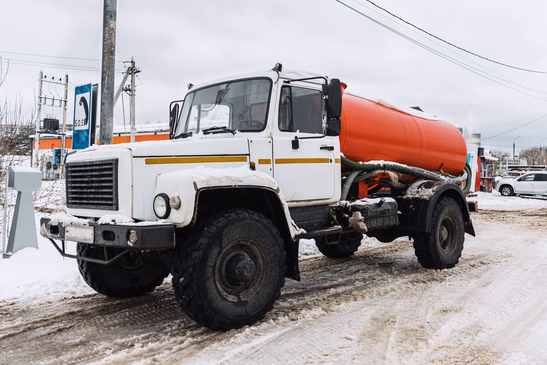 White tanker truck with orange tank on a snowy road.