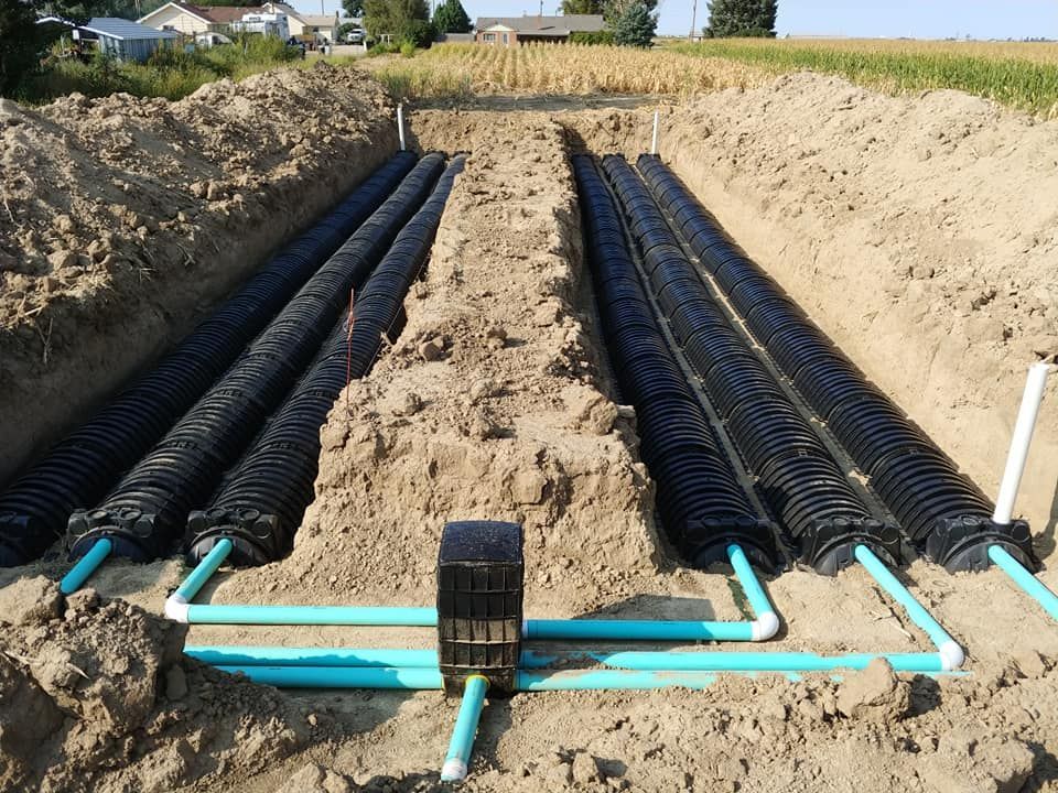 A row of black pipes are sitting in the dirt.