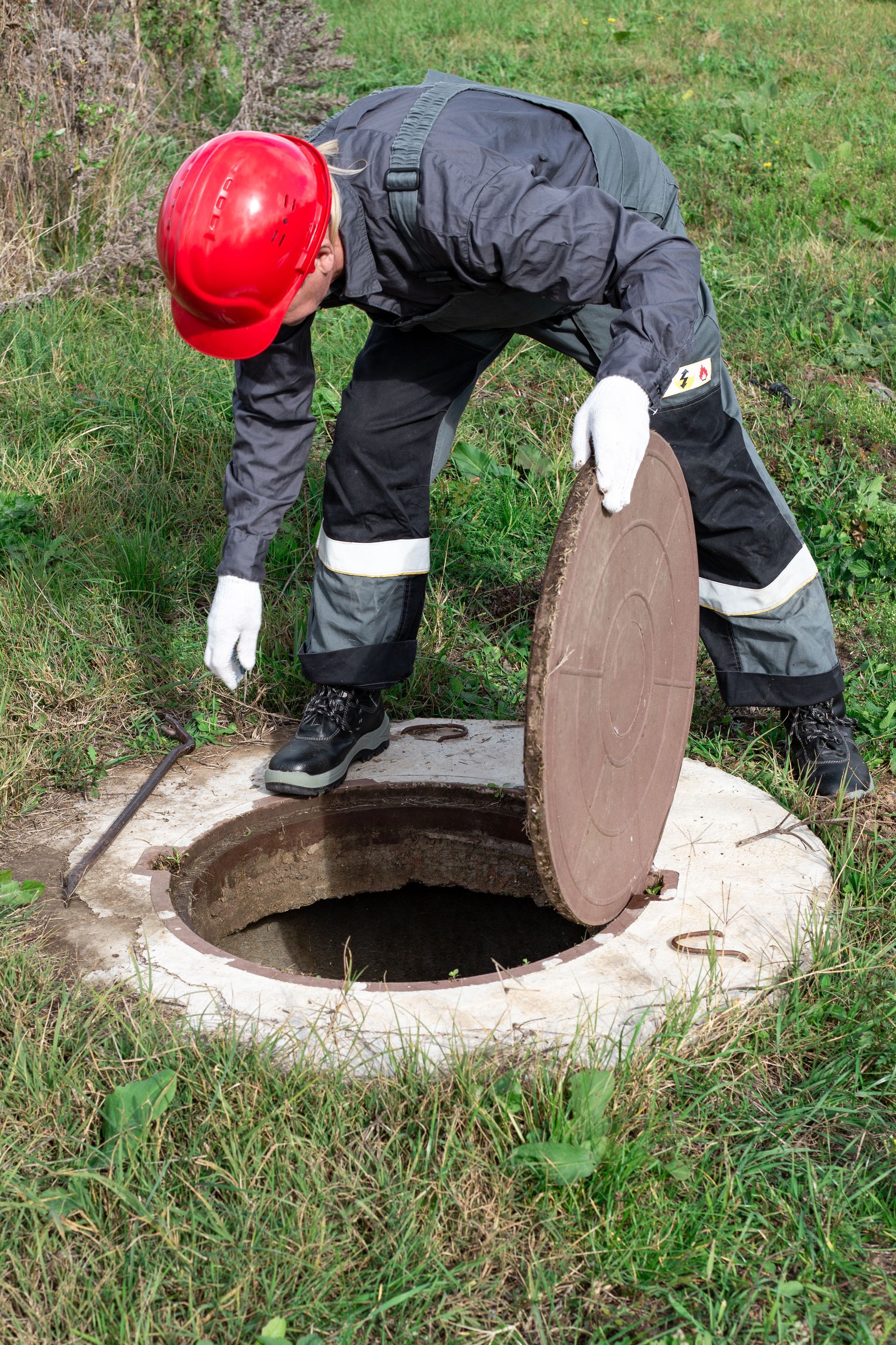 a man is standing in the grass next to a septic tank with the lid open .
