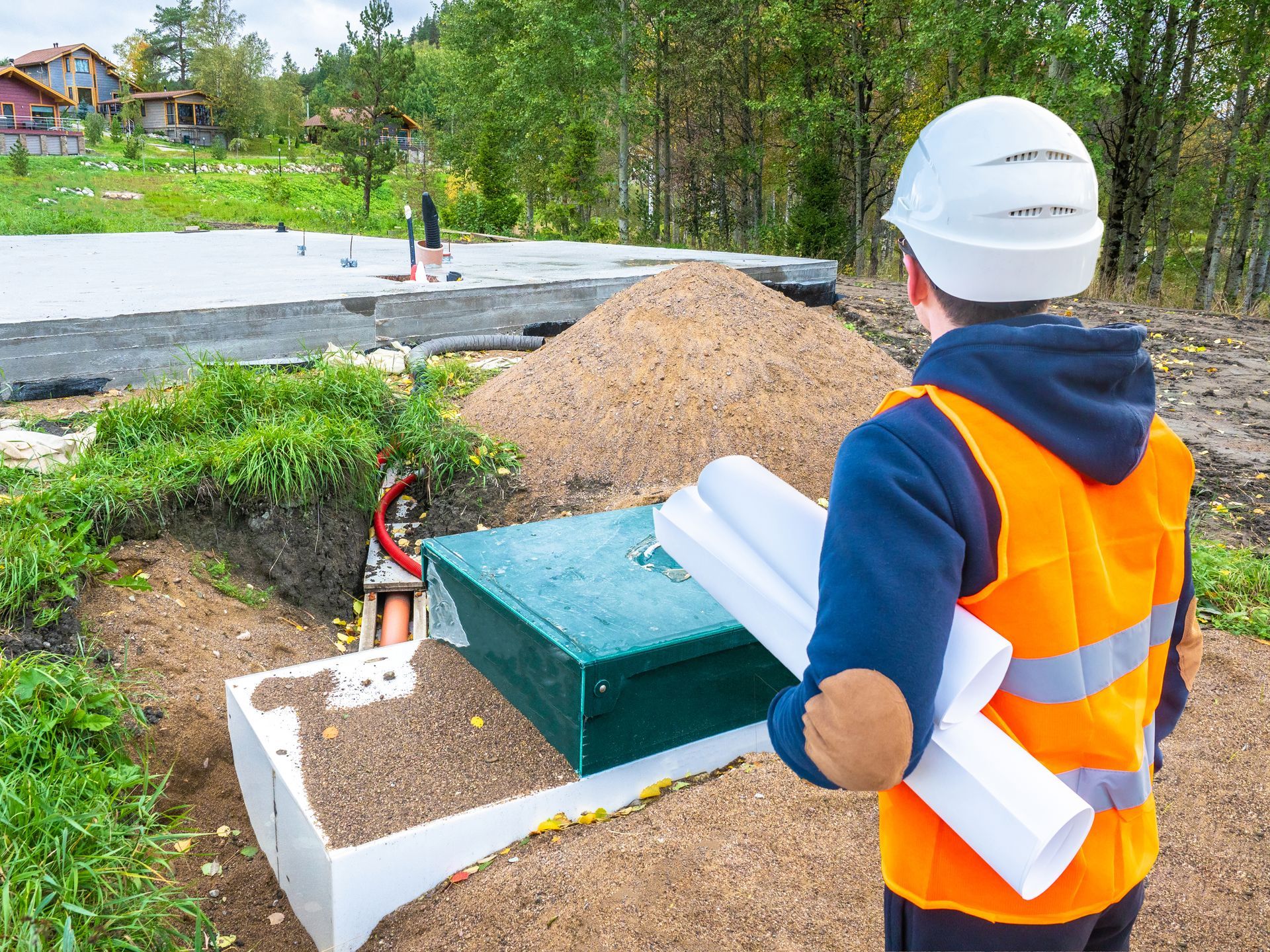 a man in an orange vest and hard hat is holding blueprints in front of a construction site .