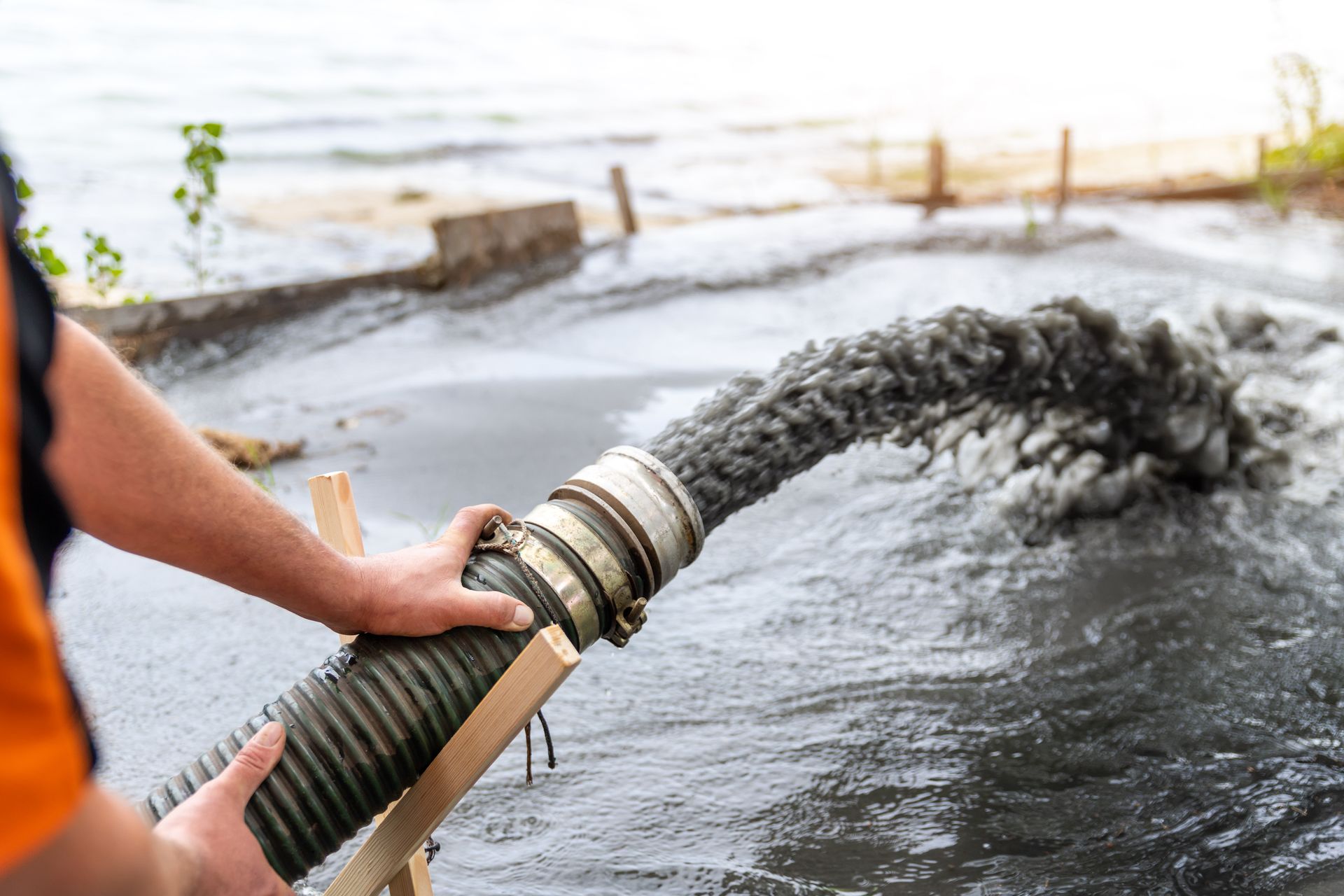 a man is pumping water from a hose into a body of water .