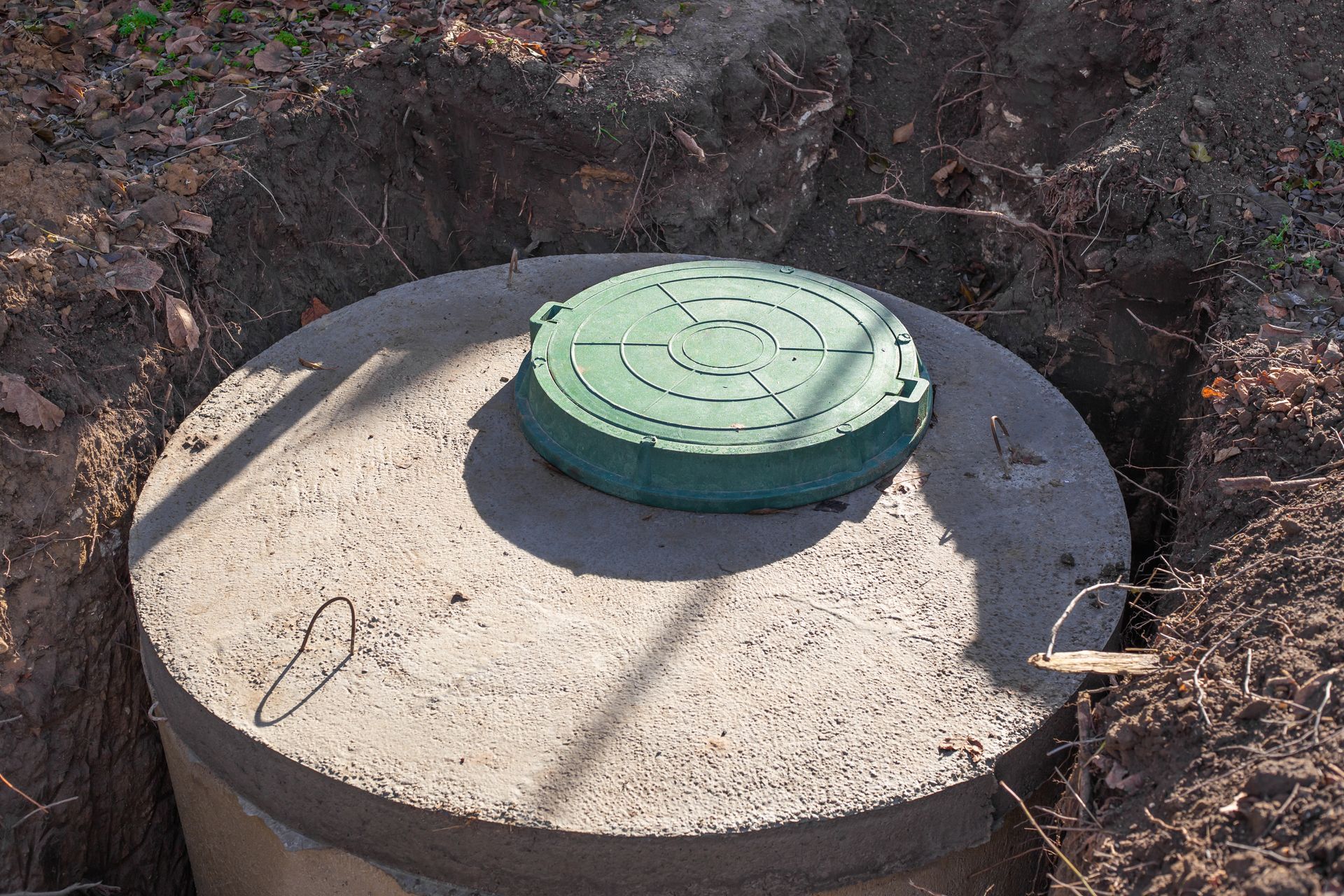 A concrete septic tank with a green lid is sitting in the dirt.