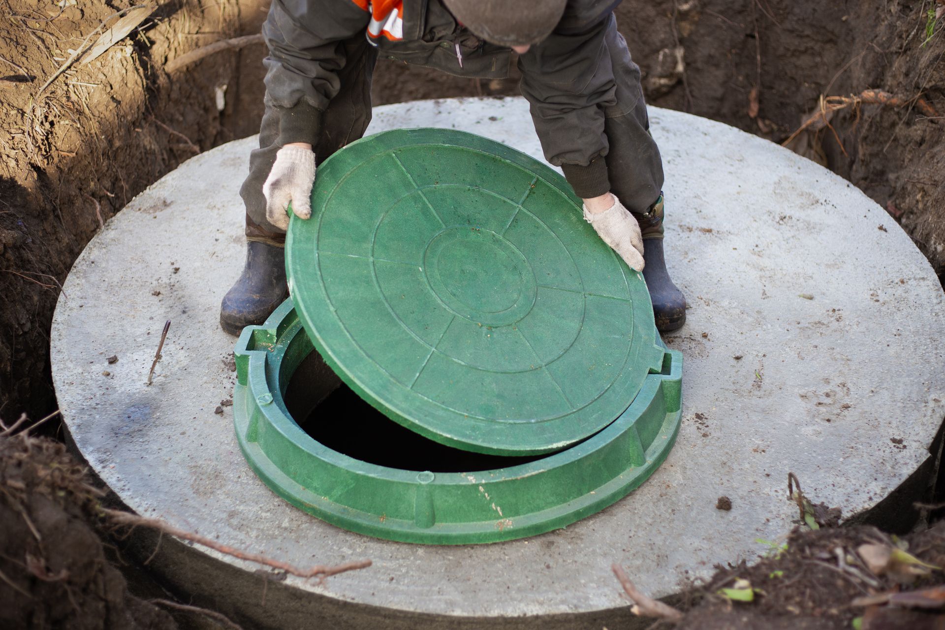 A man is opening a green manhole cover on a concrete circle.