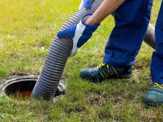 a man is using a vacuum hose to clean a septic tank .