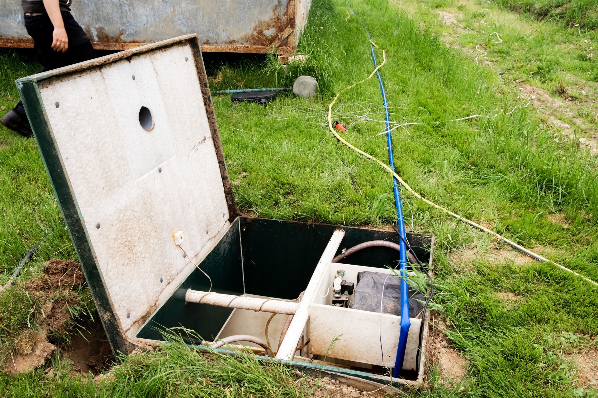 a man is standing in the grass next to a septic tank with the lid open .