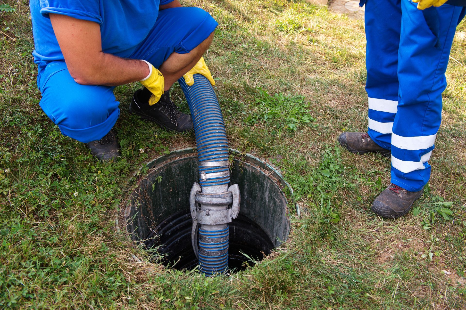 a man is kneeling down next to a manhole cover with a hose coming out of it .