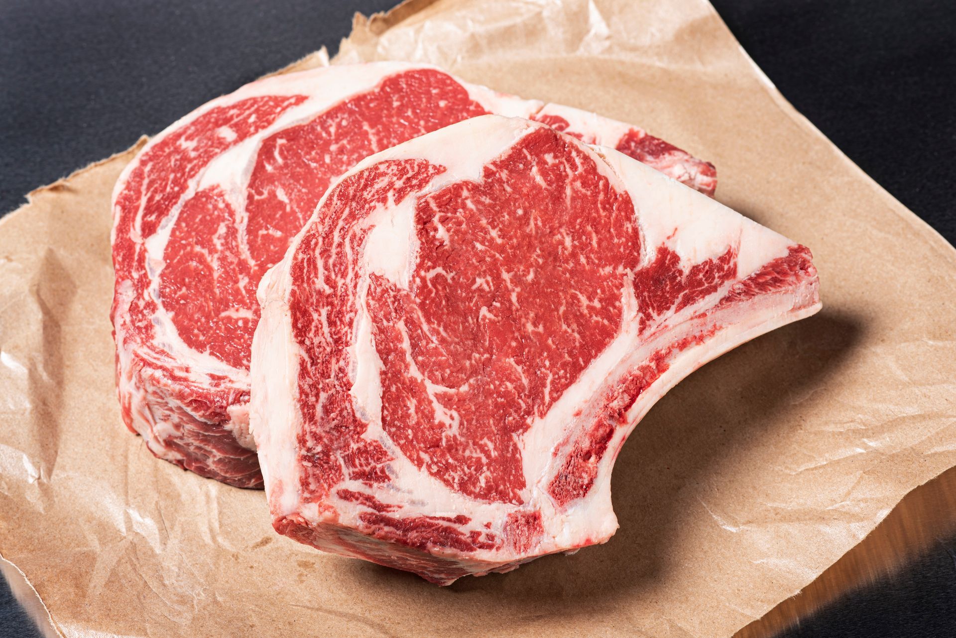 Three steaks are sitting on a piece of brown paper.