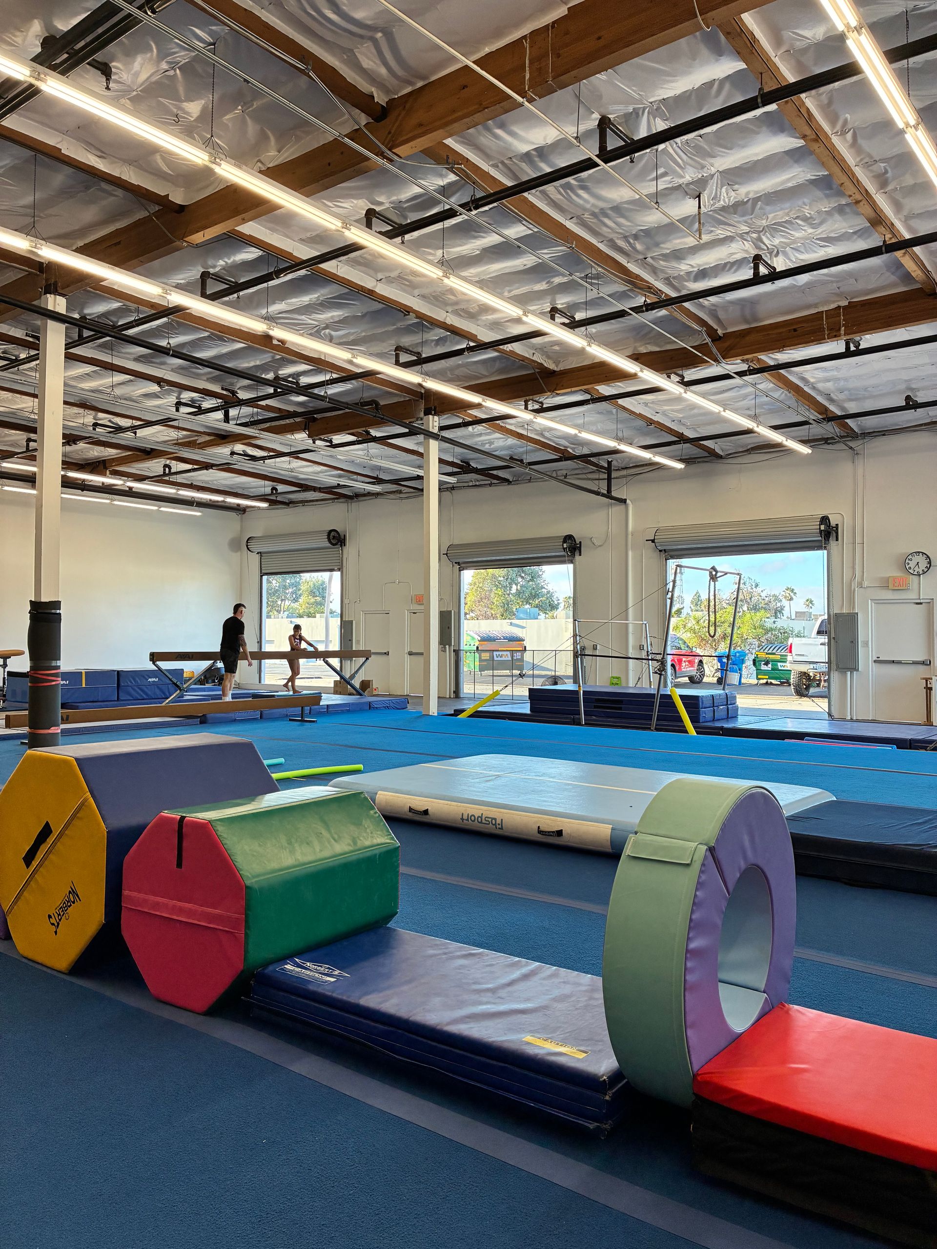 Gymnasium interior with mats, bars, and obstacles, likely for gymnastics training.