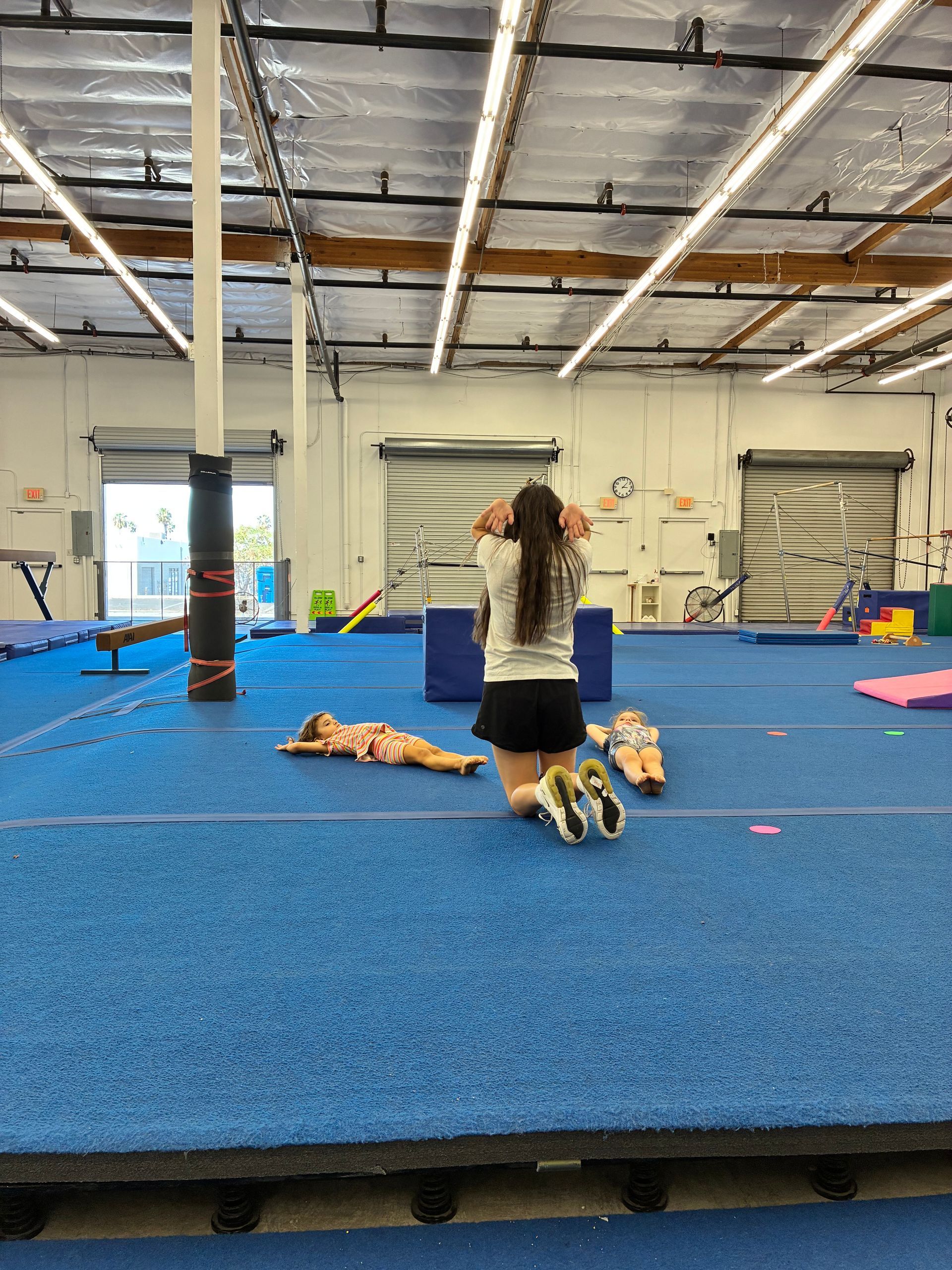 A smiling gymnastics coach with four young girls in green leotards, posing together on a mat.