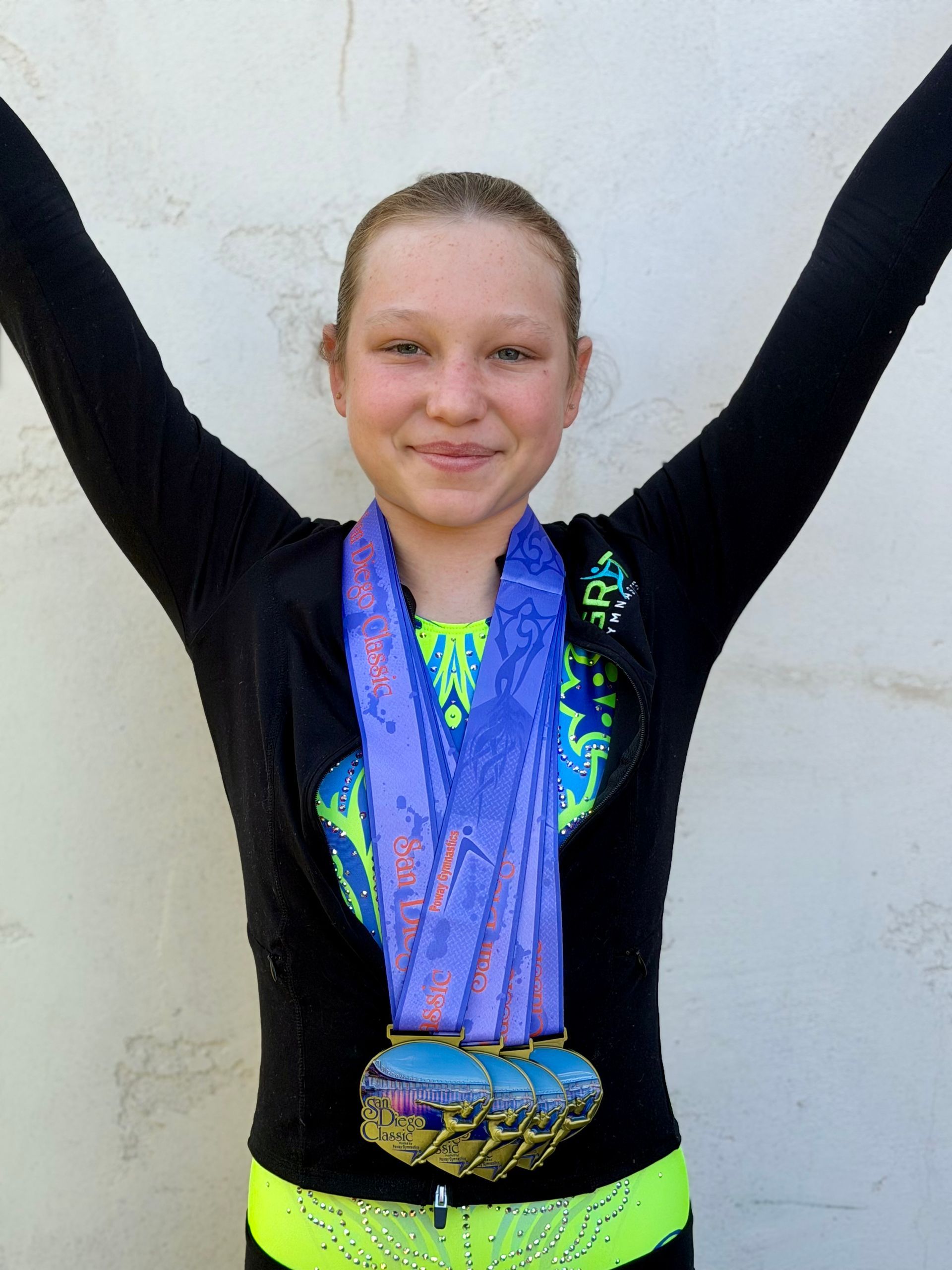 Smiling gymnastics coach with four girls in green leotards on a blue mat.
