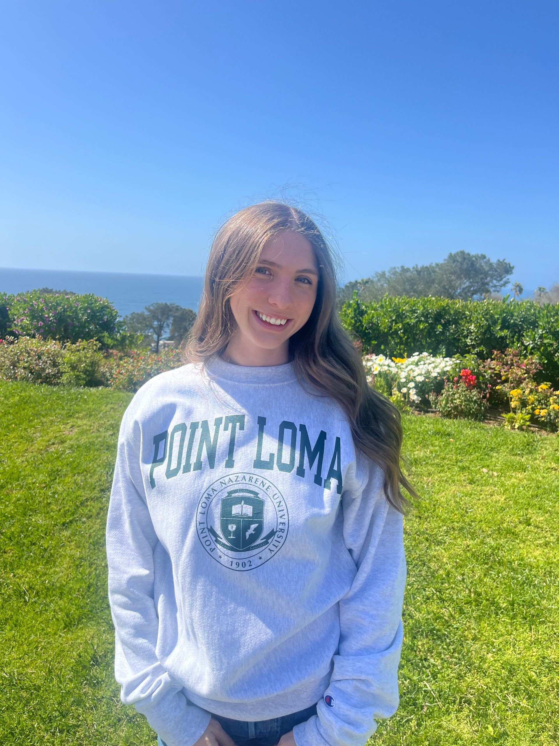 Woman in Point Loma sweatshirt smiles outdoors near ocean.